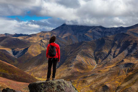 Woman Standing and Looking at Mountain Range on a Cloudy Fall Day in Canadian Nature. Taken in Tombstone Territorial Park, Yukon, Canada.の写真素材