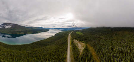 Beautiful Panoramic View of Scenic Road alongside Peaceful Lake surrounded by Mountains in Canadian...