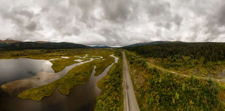 Panoramic View of Scenic Road alongside Peaceful Lake surrounded by Mountains in Canadian Nature. Aerial Drone Shot. Taken near Stewart-Cassiar Highway, Northern British Columbia, Canada.の写真素材