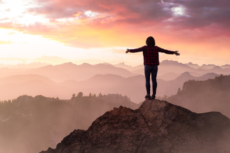 Fantasy Adventure Composite with a Girl on top of a Mountain Cliff with Dramatic Landscape in Background. Landscape from British Columbia, Canada. Dramatic Stormy Sunset Sky.の写真素材