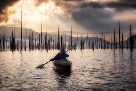 Adventurous Girl kayaking on an infatable kayak in a beautiful lake. Colorful peaceful Sunrise Art Render. Taken in Stave Lake, East of Vancouver, British Columbia, Canada. Adventure, vacation conceptの写真素材
