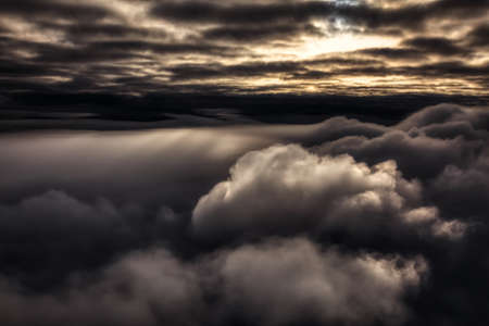 Cloudscape Background. Beautiful and striking aerial view of the puffy clouds. Dramatic Dark Art Render. Taken over the mountains from airplane near Vancouver, British Columbia, Canada.の写真素材