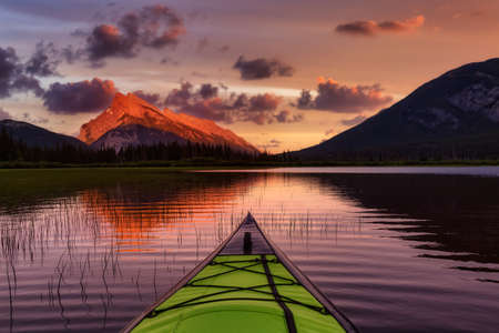 Kayaking in a beautiful lake surrounded by the Canadian Mountain Landscape. Colorful Sunset Sky Art Render. Vermilion Lakes, Banff, Alberta, Canada.の写真素材