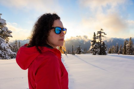 Adventurous White Caucasian Woman hiking outdoors in snow on top of mountain. Sunny Spring Sumset...