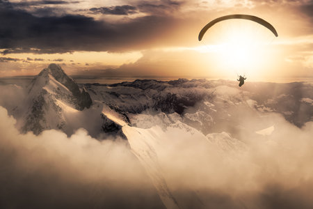Adventure Composite Image of Paraglider Flying up high in the Rocky Mountains. Sunny Sunset Sky. Aerial Background from British Columbia, Canada. Extreme Sport Conceptの写真素材