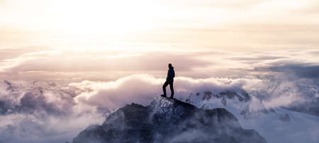 Magical Fantasy Adventure Image Composite of Man Hiking on top of a rocky mountain peak. Background Landscape from British Columbia, Canada. Colorful Sunset or Sunrise Colorful Skyの素材 [FY310170439299]