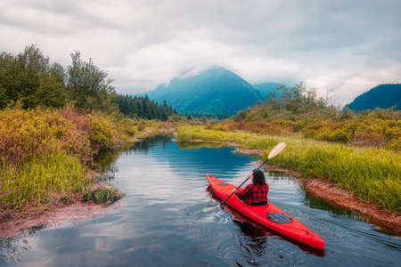Adventure Caucasian Adult Woman Kayaking in Red Kayak surrounded by Canadian Mountain Landscape. Artistic Color Render. Taken in Widgeon Valley, Pitt Meadows, Vancouver, British Columbia, Canada.の写真素材