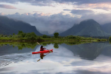 Adventure Caucasian Adult Woman Kayaking in Red Kayak surrounded by Canadian Mountain Landscape. Sunset Sky Art Render. Widgeon Valley, Pitt Meadows, Vancouver, British Columbia, Canada.の写真素材