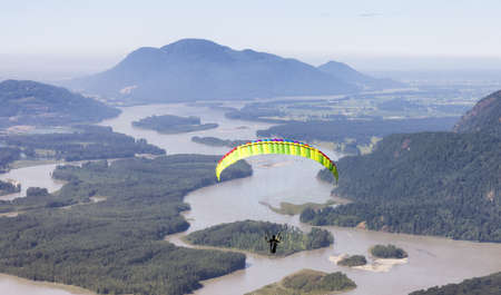 Adventurous Woman Flying on a paraglider around the Canadian Mountain Landscape. Harrison Mills near...