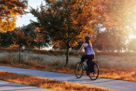 Adventurous White Caucasian Adult Woman riding a road bicycle on a bike path at the famous Stanley Park in a modern city. Sunset. Fall Colors Art Render. Downtown Vancouver, British Columbia, Canada.の写真素材