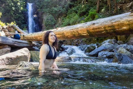 Adult Caucasian Woman hiker swimming in glacier water at Norvan Falls during hot and sunny summer day. Canadian Nature Background. Lynn Valley, North Vancouver, British Columbia, Canada.の写真素材