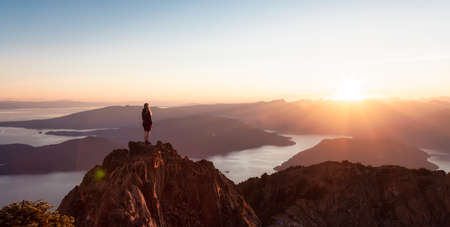 Adventurous Caucasian Woman Hiking on top of a Rocky Mountain Cliff. Sunny Summer Sunset. Mnt...