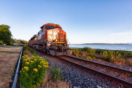 White Rock, Greater Vancouver, British Columbia, Canada - July 25, 2021: A freight train riding through the city by the beach during a colorful summer evening.のeditorial素材