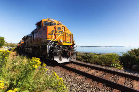 White Rock, Greater Vancouver, British Columbia, Canada - July 25, 2021: A freight train riding through the city by the beach during a colorful summer evening.のeditorial素材