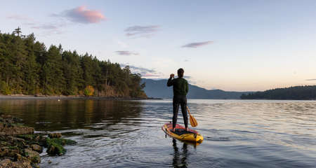 Adventurous Caucasian Adult Woman on a Stand Up Paddle Board is paddling on the West Coast of Pacific Ocean. Sunny Sunrise. Victoria, Vancouver Island, BC, Canada. Adventure Travel Conceptの写真素材