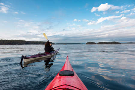 Adventurous Woman on Sea Kayak paddling in the Pacific Ocean. Blue Summer Evening Sky. Taken near Victoria, Vancouver Islands, British Columbia, Canada. Concept: Sport, Adventureの写真素材