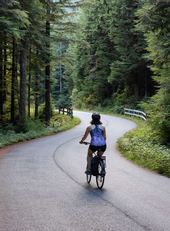 Adventurous White Caucasian Woman on a bicycle riding on a path in Green Canadian Rain Forest. Seymour Valley Trailway in North Vancouver, British Columbia, Canada.の写真素材