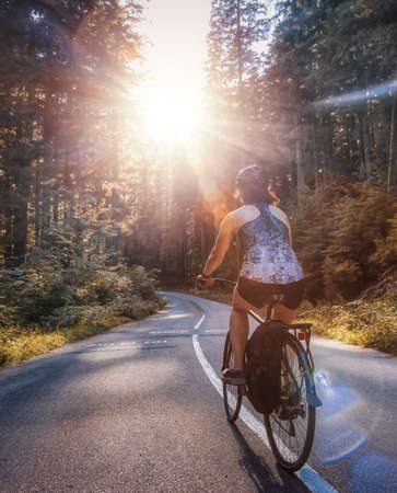 Adventurous White Caucasian Woman on a bicycle riding on a path in Green Canadian Rain Forest. Sunny Sunset. Seymour Valley Trailway in North Vancouver, British Columbia, Canada.の写真素材