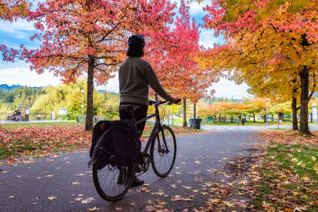 Adult Woman with bicycle on Bike Path in Stanley Park. Colorful Fall Season Trees. Downtown...