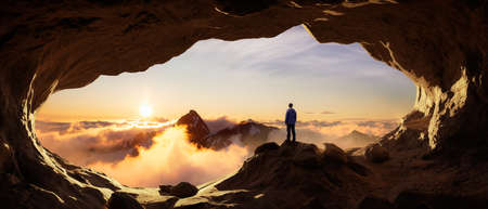 Adventurous Man Hiker standing in a cave with rocky mountains in background. Adventure Composite. 3d Rendering Peak. Aerial Image of landscape from British Columbia, Canada. Sunset Skyの写真素材