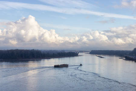 Aerial View of Tugboat in Fraser River and Mountain Landscape in background. Sunny Fall Season Day. Taken on Port Mann Bridge in Surrey, Vancouver, British Columbia, Canada.の写真素材
