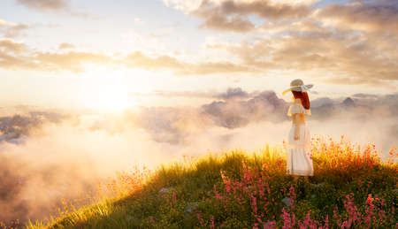 White caucasian adult woman standing in the meadows on top of a mountain wearing an elegant dress. 3d rendering art. Sunset Sky. Aerial landscape background image from British Columbia, Canada.の写真素材