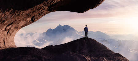 Dramatic Adventurous Scene with Man standing inside a Rocky Cave Landcspae. 3d Rendering. Sunset Sky. Aerial Mountain Image from British Columbia, Canada. Adventure Conceptの写真素材