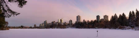 View of Lost Lagoon in famous  Park in a modern city with buildings skyline in background. Frozen Lake in Winter. Colorful Sunset Sky. Downtown Vancouver, British Columbia, Canada.の写真素材