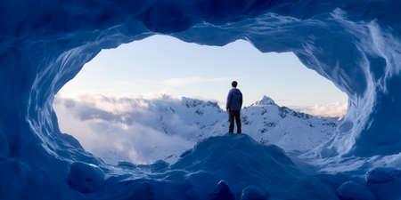 Adventurous Man Hiker standing in an Ice Cave with rocky mountains in background. Adventure Composite. 3d Rendering rocks. Aerial Image of landscape from British Columbia, Canada. Cloudy Skyの写真素材
