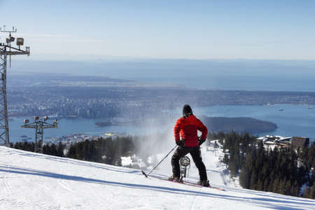 Grouse Mountain, North Vancouver, British Columbia, Canada - March 9, 2022: Skiier riding the snowy mountain with the city in background. Sunny morning.のeditorial素材