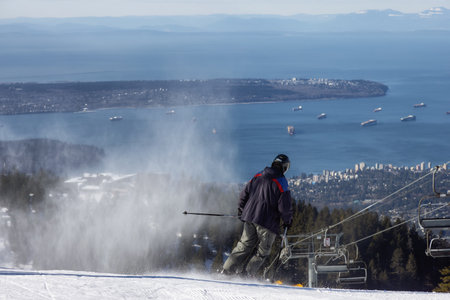 Grouse Mountain, North Vancouver, British Columbia, Canada - March 9, 2022: Skiier riding the snowy mountain with the city in background. Sunny morning.のeditorial素材