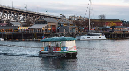 Downtown Vancouver, British Columbia, Canada - April 15, 2022: Water Taxi Boat in False Creek and Granville Island in background during sunset.のeditorial素材