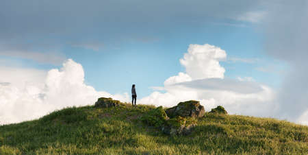 Magical fantasy scene with woman on top of hill and mountain landscape in background. 3d Rendering. Dramatic Cloudy Sky. Adventure Conceptの写真素材