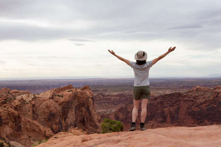 Adventurous Woman Hiking at a Desert Canyon with Red Rock Mountains. Cloudy Sky. Canyonlands...