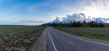 Scenic Road surrounded by Mountains and Trees in American Landscape. Sunset Sky in Spring Season. Grand Teton National Park. Wyoming, United States. Nature Background Panoramaの写真素材