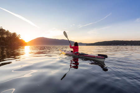 Adventurous Woman on Sea Kayak paddling in the Pacific Ocean. Sunny Summer Sunset. Taken near Victoria, Vancouver Islands, British Columbia, Canada. Concept: Sport, Adventureの写真素材