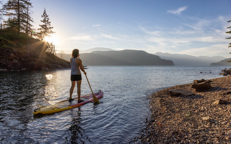 Adventurous Woman Paddling on a Paddle Board in a peaceful lake. Sunny Sunset. Harrison Hot Springs, British Columbia, Canada. Adventure Sport Travel Conceptの写真素材