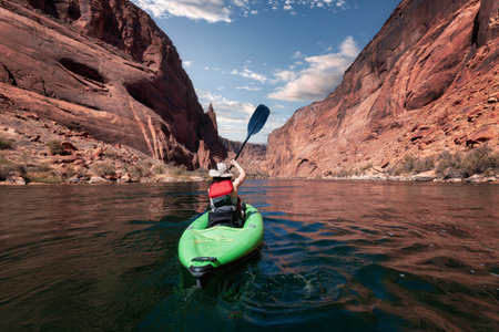 Adventurous Woman on a Kayak paddling in Colorado River. Glen Canyon, Arizona, United States of America. American Mountain Cloudy Sky Art Render. Adventure Travelの写真素材