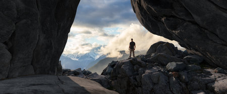 Adventurous Man Standing in cave on top of Mountain. Extreme Adventure Composite. 3d Rendering Peak. Background Aerial Image from British Columbia, Canada.の写真素材