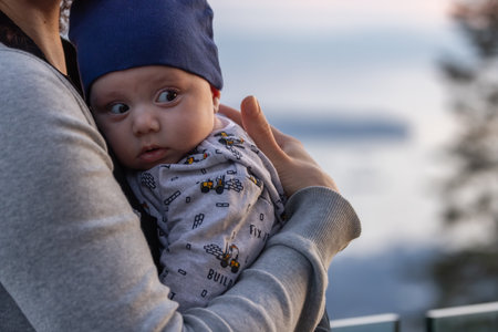Newborn baby boy in mothers arms outdoors in nature during sunset. Vancouver, BC, Canada.