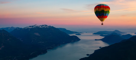 Hot Air Balloon flying over Canadian Mountain Landscape on the West Coast of Pacific Ocean. Aerial Nature Background. Sunset Sky. Howe Sound, BC, Canada.の写真素材