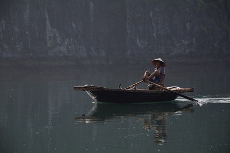 Vietnamese guy paddling with His feet on a boat in a floating village inside Halong Bay, Vietnamのeditorial素材