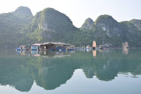 Floating houses with green mountains reflecting in the water in Halong Bay, Vietnamの写真素材