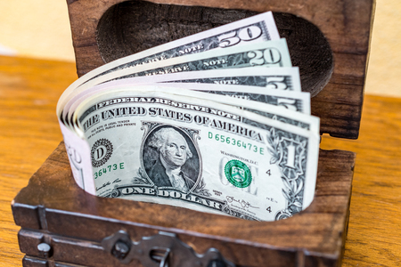 Vintage wooden box full of money: folded and spreaded US dollar banknotes in a chest on wooden...