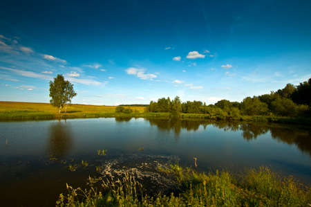 Countryside landscape with deep blue sky and smooth lake surfaceの写真素材