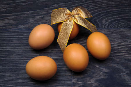 Close-up of brown Easter eggs tied by gold ribbon over dark wooden background