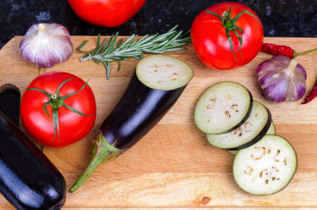 Set of vegetables on cutting board, eggplant, garlic, tomatoes, rosemary, chili pepper
