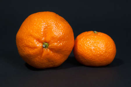 Two big and small tangerine on black backgroundの写真素材