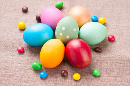 Group of colorful Easter eggs and colored candies lying on linen fabric cloth close up