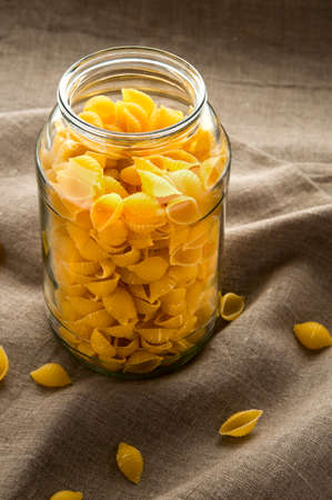 Shell macaroni pasta in glass bowl on hessian fabric cloth backgroundの写真素材